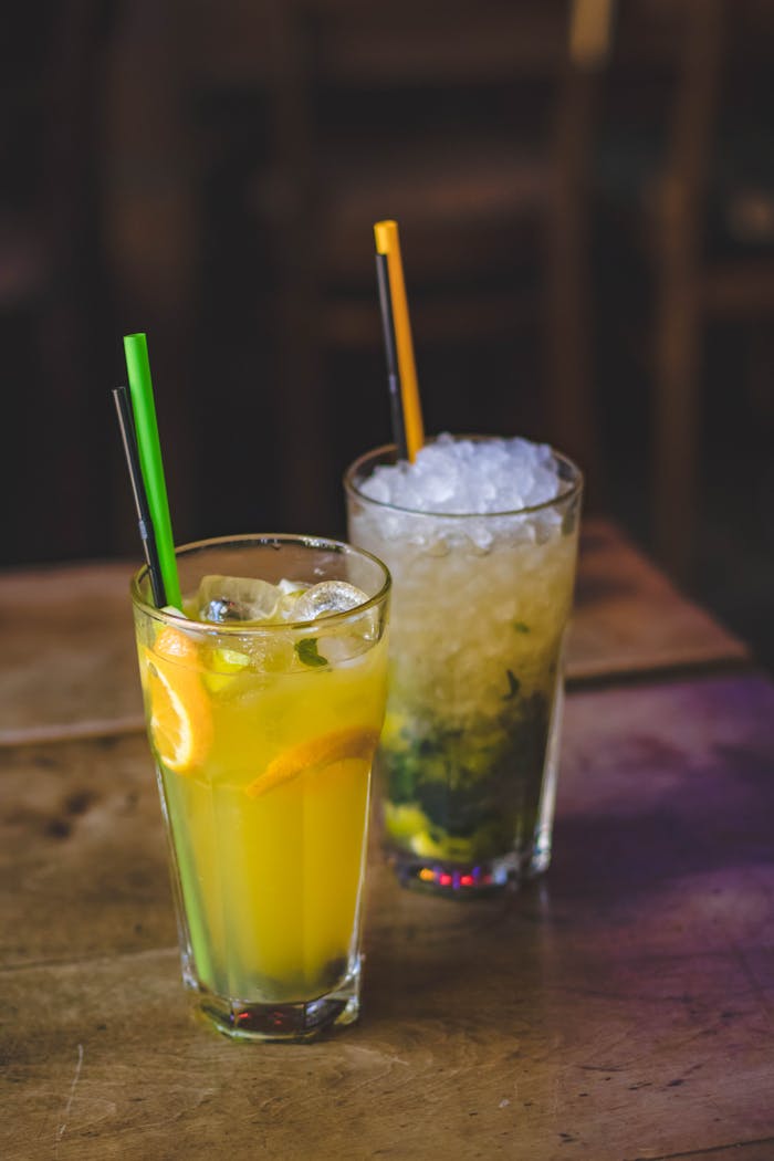 Close-up of colorful citrus and mint cocktails with ice and straws on a wooden table indoors.